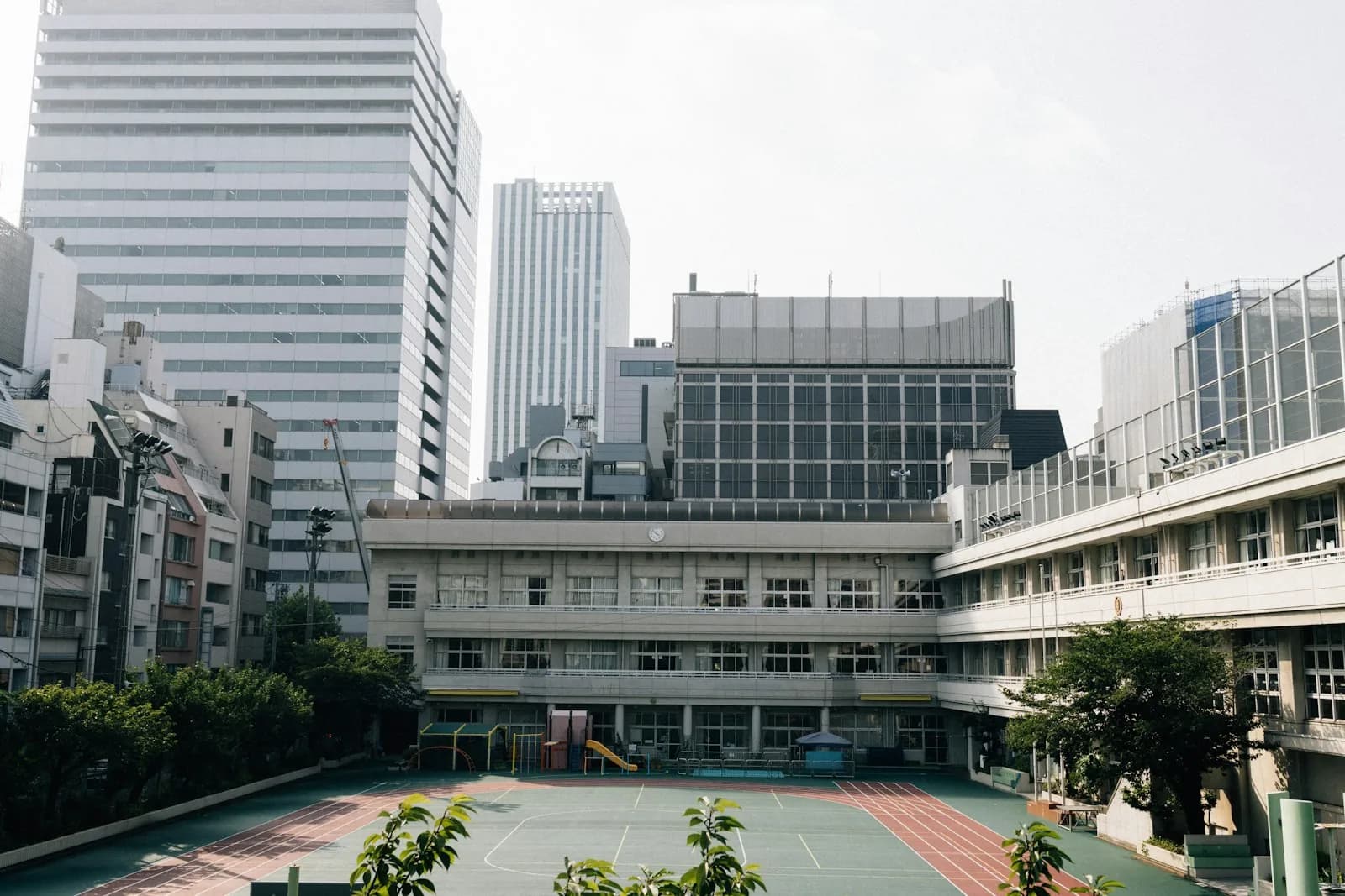 Modern elementary school building with athletic courtyard and playground, no people in frame