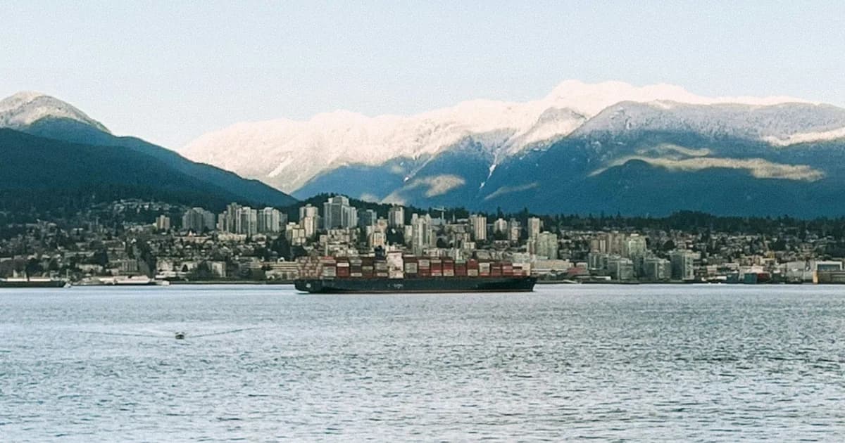 Snow-capped North Shore mountains above the North Vancouver waterfront skyline, with a loaded container ship crossing Burrard Inlet in the foreground