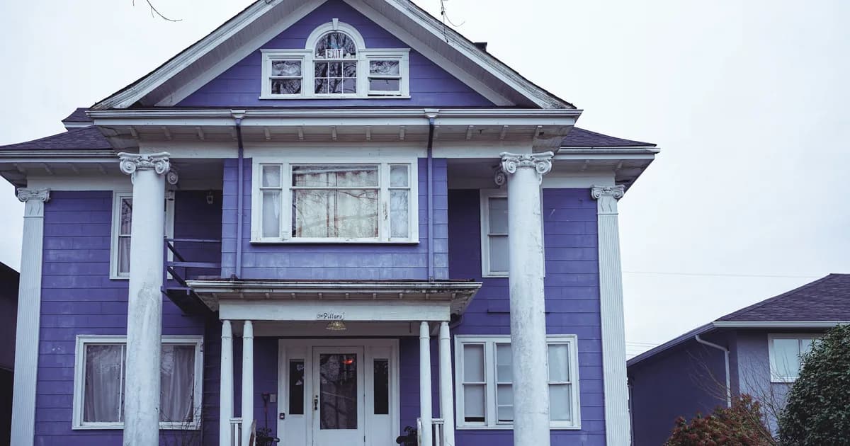 Edwardian-era Vancouver heritage house painted purple with white trim, tall Ionic columns, and a covered front porch on an overcast day