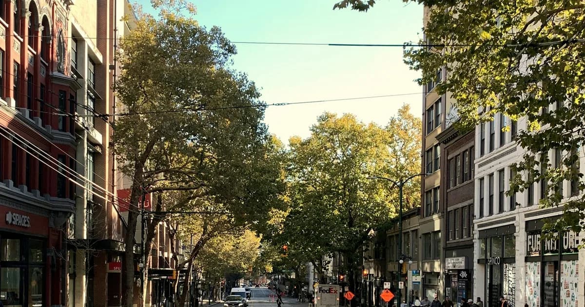 Tree-lined Vancouver street with brick and stone mid-rise buildings on both sides under a clear sky in early autumn
