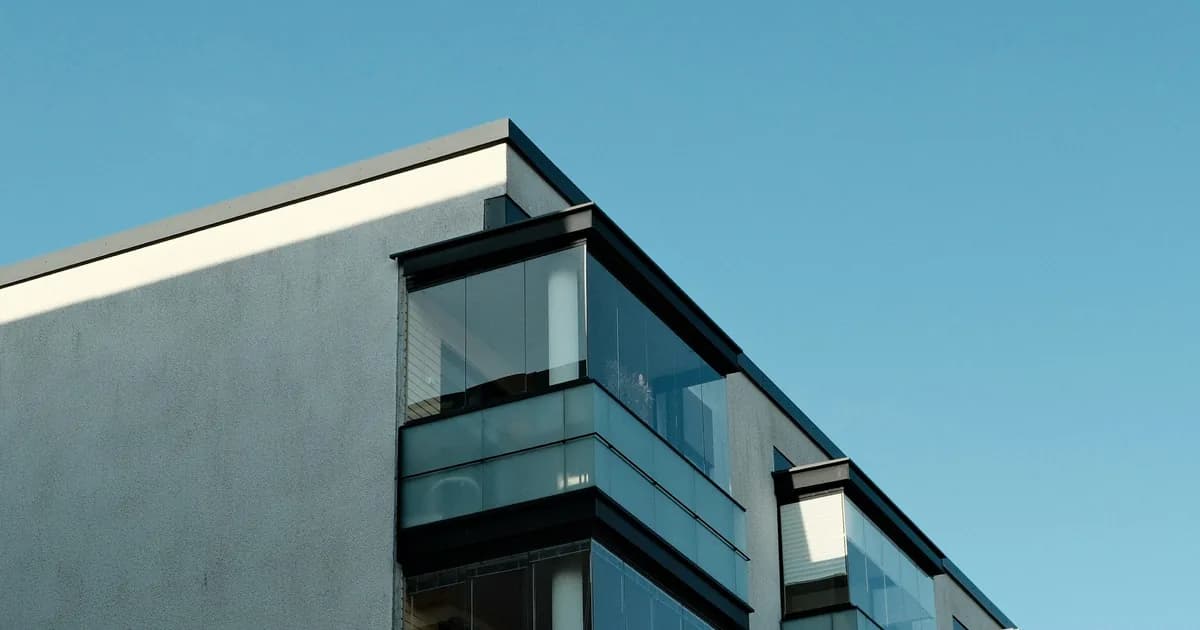 Modern multi-story apartment building with glass-enclosed balconies under a clear blue sky