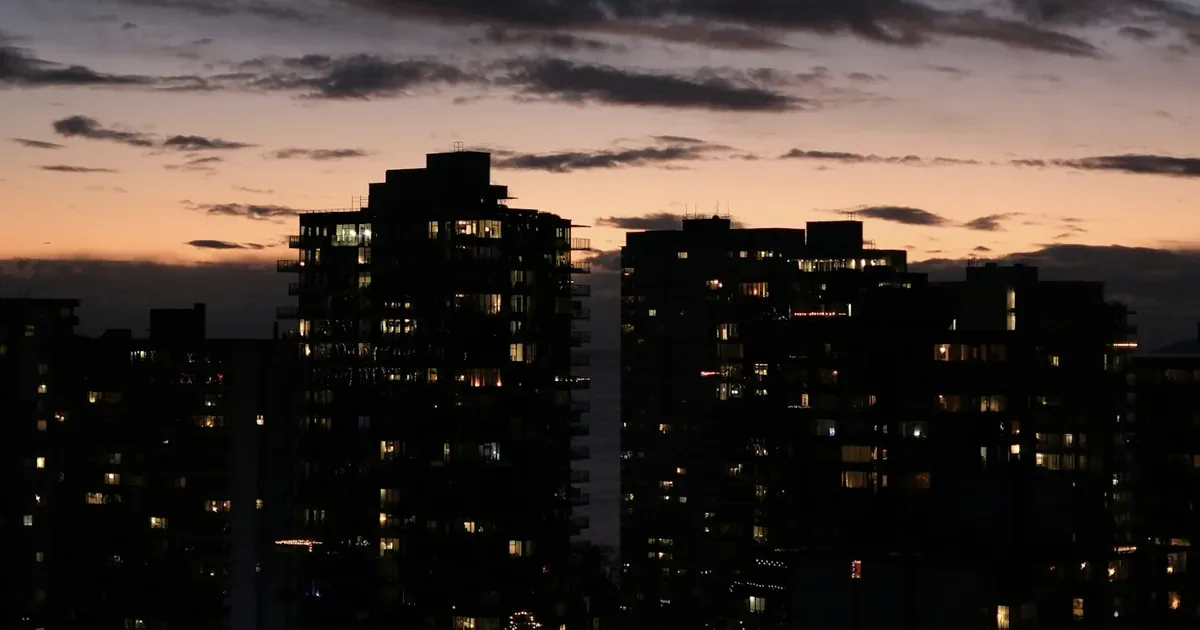 Vancouver residential apartment towers silhouetted against an orange and blue sky at dusk, with a few windows lit